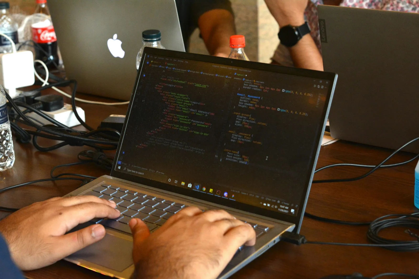 Mâini pe tastatura unui laptop, cu cod pe ecran